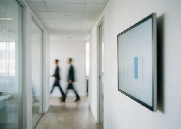 A wall-mounted dashboard in an office corridor, out of focus, no legible numbers